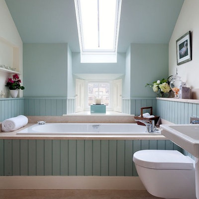 Example of a transitional stone tile limestone floor and beige floor drop-in bathtub design in Other with a wall-mount sink, a wall-mount toilet and blue walls
