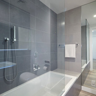 Bathroom - large contemporary master gray tile and porcelain tile medium tone wood floor and beige floor bathroom idea in New York with a one-piece toilet, flat-panel cabinets, white cabinets, white walls, an integrated sink and glass countertops
