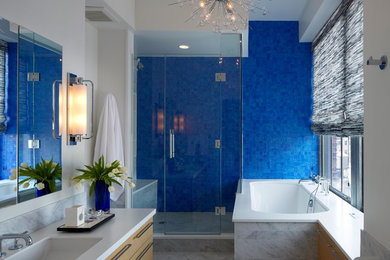 Foto de cuarto de baño actual con lavabo bajoencimera, armarios con paneles lisos, puertas de armario de madera clara, bañera encastrada sin remate, ducha esquinera, baldosas y/o azulejos azules y paredes blancas