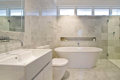 サンディエゴにある高級な広いコンテンポラリースタイルのおしゃれなマスターバスルーム (フラットパネル扉のキャビネット、白いキャビネット、置き型浴槽、アルコーブ型シャワー、白いタイル、石タイル、白い壁、大理石の床、横長型シンク、一体型トイレ	、グレーの床、開き戸のシャワー) の写真