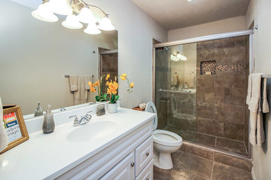 ダラスにあるコンテンポラリースタイルのおしゃれな浴室 (レイズドパネル扉のキャビネット、白いキャビネット、茶色いタイル、白い壁、クオーツストーンの洗面台、ベージュの床、引戸のシャワー、ベージュのカウンター) の写真