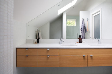 Modern bathroom in Auckland with light wood cabinets, porcelain flooring and marble worktops.