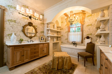 ヒューストンにあるラグジュアリーなシャビーシック調のおしゃれな浴室 (中間色木目調キャビネット、置き型浴槽、オーバーカウンターシンク、レイズドパネル扉のキャビネット) の写真