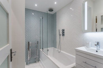 Small contemporary shower room bathroom in London with flat-panel cabinets, white cabinets, a built-in bath, a shower/bath combination, a wall mounted toilet, grey tiles, white walls, porcelain flooring, a built-in sink, tiled worktops and white floors.