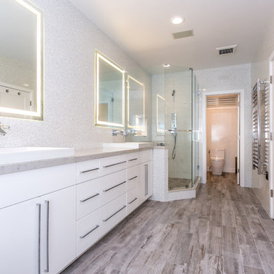 Example of a large minimalist master beige tile and porcelain tile porcelain tile and brown floor bathroom design in Los Angeles with a drop-in sink, white cabinets, a wall-mount toilet, white walls, flat-panel cabinets, marble countertops and a hinged shower door