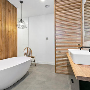 Inredning av ett modernt mellanstort beige beige en-suite badrum, med släta luckor, svarta skåp, ett fristående badkar, en öppen dusch, vit kakel, keramikplattor, vita väggar, cementgolv, ett fristående handfat, träbänkskiva, grått golv och med dusch som är öppen