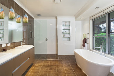 Modernes Badezimmer mit flächenbündigen Schrankfronten, braunen Schränken, freistehender Badewanne, Eckdusche, braunen Fliesen, weißer Wandfarbe, Einbauwaschbecken, braunem Boden, offener Dusche und weißer Waschtischplatte in Sonstige