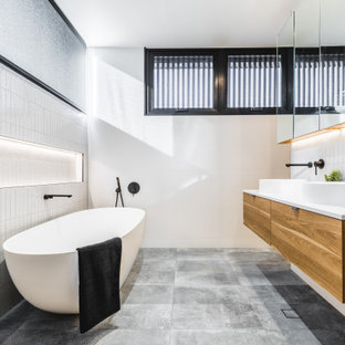 Photo of a contemporary bathroom in Other with flat-panel cabinets, medium wood cabinets, a freestanding tub, white tile, white walls, a vessel sink, grey floor, white benchtops, a double vanity, a floating vanity and a niche.