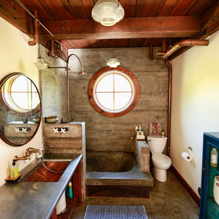 Immagine di una stanza da bagno con doccia industriale di medie dimensioni con nessun'anta, ante in legno scuro, doccia aperta, WC a due pezzi, pareti gialle, lavabo sottopiano, vasca da incasso, pavimento in cemento, top in acciaio inossidabile, doccia aperta, piastrelle in gres porcellanato, pavimento marrone e top grigio