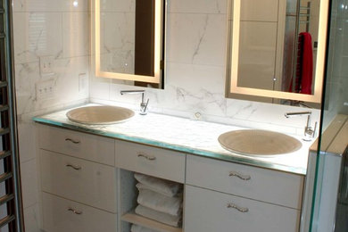 Modelo de cuarto de baño actual con baldosas y/o azulejos blancos, baldosas y/o azulejos de mármol, lavabo sobreencimera, encimera de vidrio y ducha con puerta con bisagras