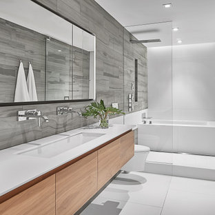Foto di una stanza da bagno padronale design di medie dimensioni con ante lisce, ante in legno scuro, zona vasca/doccia separata, WC sospeso, piastrelle di pietra calcarea, lavabo sottopiano, top in superficie solida, pavimento bianco, porta doccia a battente, top bianco, vasca sottopiano e piastrelle grigie