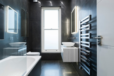 Inspiration for a medium sized modern family bathroom in London with flat-panel cabinets, white cabinets, a built-in bath, a shower/bath combination, a wall mounted toilet, black tiles, porcelain tiles, black walls, porcelain flooring, a console sink, wooden worktops, black floors, a hinged door, white worktops, a wall niche, a single sink, a floating vanity unit and a drop ceiling.