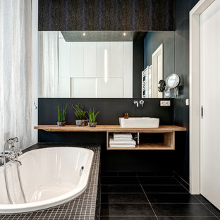 Kleines Modernes Badezimmer En Suite mit offenen Schränken, braunen Schränken, Einbaubadewanne, schwarzer Wandfarbe, Aufsatzwaschbecken, Waschtisch aus Holz, schwarzem Boden und brauner Waschtischplatte in Berlin