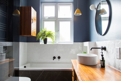 Cette image montre une petite salle de bain principale traditionnelle avec des portes de placard marrons, une baignoire posée, un espace douche bain, WC suspendus, un carrelage blanc, des carreaux de porcelaine, un mur bleu, un sol en carrelage de porcelaine, un plan de toilette en bois, un sol noir, un plan de toilette marron, meuble simple vasque, meuble-lavabo sur pied, un plafond en bois et un placard à porte plane.