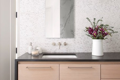 Esempio di una stanza da bagno moderna con ante lisce, ante in legno chiaro, piastrelle grigie, piastrelle bianche, piastrelle a mosaico, pareti multicolore, pavimento in laminato, lavabo sottopiano e top in superficie solida