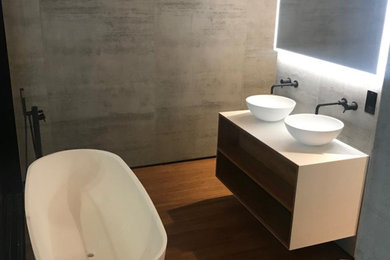 Medium sized contemporary family bathroom in Other with open cabinets, white cabinets, a freestanding bath, travertine tiles, grey walls, light hardwood flooring, a vessel sink, concrete worktops, brown floors, white worktops, double sinks and a floating vanity unit.