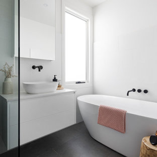 Design ideas for a mid-sized modern master bathroom in Melbourne with flat-panel cabinets, white cabinets, a freestanding tub, a corner shower, a one-piece toilet, white tile, ceramic tile, white walls, ceramic floors, a console sink, engineered quartz benchtops, black floor, a hinged shower door, white benchtops, a single vanity and a floating vanity.