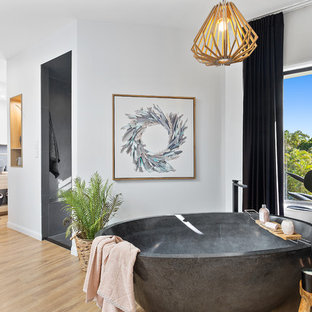 This is an example of a contemporary master bathroom in Brisbane with flat-panel cabinets, light wood cabinets, a freestanding tub, black tile, light hardwood floors, a vessel sink, wood benchtops, beige floor and beige benchtops.