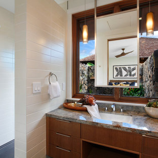 Mid-sized island style white tile and porcelain tile gray floor bathroom photo in Hawaii with flat-panel cabinets, medium tone wood cabinets, white walls, an undermount sink, granite countertops and multicolored countertops