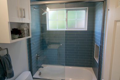 Источник вдохновения для домашнего уюта: ванная комната среднего размера в стиле модернизм с фасадами в стиле шейкер, белыми фасадами, ванной в нише, душем над ванной, унитазом-моноблоком, синей плиткой, керамической плиткой, белыми стенами, полом из керамической плитки, монолитной раковиной, столешницей из искусственного камня, разноцветным полом, душем с раздвижными дверями и белой столешницей