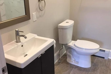 Example of a mid-sized transitional 3/4 white tile and porcelain tile beige floor and porcelain tile bathroom design in New York with flat-panel cabinets, black cabinets, a two-piece toilet, white walls and an integrated sink