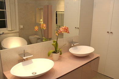 This is an example of a contemporary bathroom in London with a vessel sink, a freestanding bath, a one-piece toilet and pink walls.