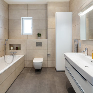 Inspiration for a medium sized modern bathroom in London with flat-panel cabinets, white cabinets, a corner bath, a wall mounted toilet, beige tiles, beige walls, a wall-mounted sink and brown floors.
