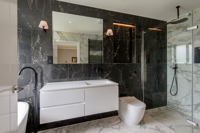 ロンドンにあるコンテンポラリースタイルのおしゃれな浴室 (フラットパネル扉のキャビネット、白いキャビネット、置き型浴槽、バリアフリー、一体型トイレ	、一体型シンク、白い床、開き戸のシャワー、白い洗面カウンター) の写真