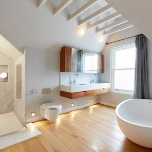 Diseño de cuarto de baño principal, actual, grande, con puertas de armario de madera oscura, bañera exenta, ducha abierta, sanitario de pared, losas de piedra, encimera de mármol, armarios con paneles lisos, paredes blancas, suelo de madera en tonos medios, lavabo bajoencimera y ducha abierta