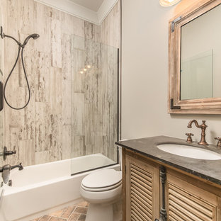Mittelgroßes Industrial Badezimmer mit Lamellenschränken, hellen Holzschränken, Badewanne in Nische, Duschbadewanne, Wandtoilette mit Spülkasten, grauen Fliesen, Porzellanfliesen, grauer Wandfarbe, Backsteinboden, Unterbauwaschbecken und Beton-Waschbecken/Waschtisch in Sonstige