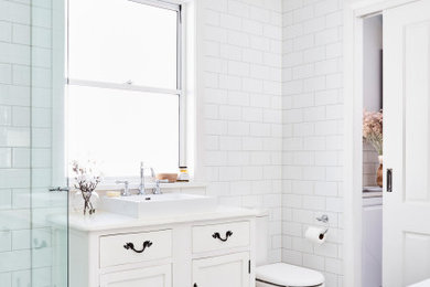 Идея дизайна: большая главная ванная комната в стиле неоклассика (современная классика) с белыми фасадами, отдельно стоящей ванной, угловым душем, раздельным унитазом, белой плиткой, плиткой кабанчик, настольной раковиной, разноцветным полом, душем с распашными дверями, белой столешницей и фасадами в стиле шейкер