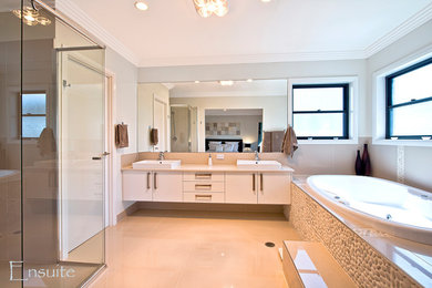 На фото: большая главная ванная комната в современном стиле с белыми фасадами, бежевой плиткой, керамогранитной плиткой, столешницей из искусственного кварца и накладной ванной с