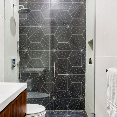 Walk-in shower - mid-sized contemporary kids' gray tile and porcelain tile porcelain tile, gray floor and single-sink walk-in shower idea in New York with flat-panel cabinets, medium tone wood cabinets, a one-piece toilet, white walls, an integrated sink, solid surface countertops, a hinged shower door, white countertops and a floating vanity