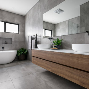 Design ideas for a contemporary bathroom in Sydney with flat-panel cabinets, medium wood cabinets, a freestanding tub, gray tile, a vessel sink, grey floor and white benchtops.
