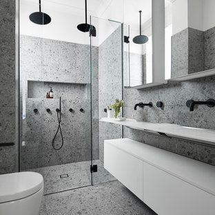 Mid-sized contemporary master bathroom in Melbourne with white cabinets, a double shower, a wall-mount toilet, gray tile, stone slab, grey walls, terrazzo floors, a wall-mount sink, laminate benchtops, grey floor, a hinged shower door, white benchtops and furniture-like cabinets.
