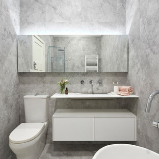 Photo of a small contemporary 3/4 bathroom in Melbourne with white cabinets, a freestanding tub, a corner shower, a wall-mount toilet, gray tile, stone tile, grey walls, marble floors, a console sink, laminate benchtops, grey floor, a hinged shower door, white benchtops and furniture-like cabinets.