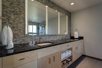 Corner shower - contemporary multicolored tile and glass tile corner shower idea in Seattle with flat-panel cabinets, light wood cabinets, beige walls, an undermount sink, granite countertops, a hinged shower door and black countertops