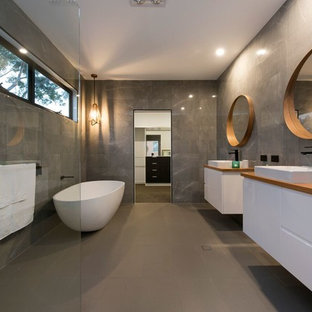 Inspiration for a contemporary master bathroom in Brisbane with flat-panel cabinets, white cabinets, a freestanding tub, a corner shower, gray tile, grey walls, a vessel sink, wood benchtops, grey floor, an open shower and brown benchtops.