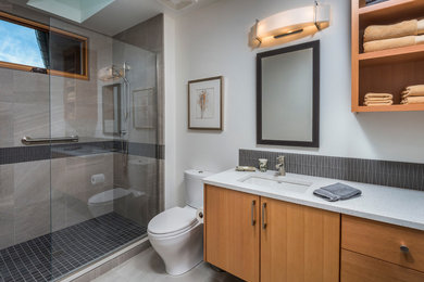 Photo of a medium sized contemporary shower room bathroom in Portland with a submerged sink, flat-panel cabinets, medium wood cabinets, engineered stone worktops, an alcove shower, a one-piece toilet, grey tiles, glass tiles, grey walls and porcelain flooring.