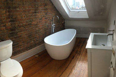 Freestanding bathtub - mid-sized industrial medium tone wood floor freestanding bathtub idea in Phoenix with shaker cabinets, white cabinets, a two-piece toilet, white walls, an integrated sink and quartz countertops