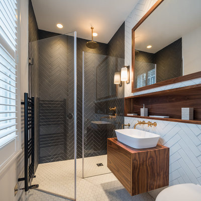 Mid-sized trendy black and white tile white floor doorless shower photo in Kent with flat-panel cabinets, brown cabinets, a vessel sink, a hinged shower door, a wall-mount toilet, white walls, wood countertops and brown countertops