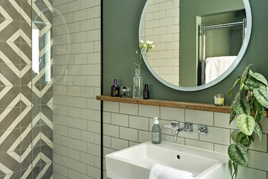 ロンドンにある中くらいなモダンスタイルのおしゃれなバスルーム (浴槽なし) (フラットパネル扉のキャビネット、青いキャビネット、オープン型シャワー、壁掛け式トイレ、グレーのタイル、セメントタイル、緑の壁、磁器タイルの床、壁付け型シンク、木製洗面台、黒い床、オープンシャワー、ブラウンの洗面カウンター) の写真