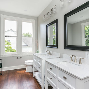 Foto de cuarto de baño principal, tradicional renovado, con armarios tipo mueble, puertas de armario blancas, bañera exenta, ducha empotrada, sanitario de dos piezas, baldosas y/o azulejos grises, paredes grises, suelo de madera oscura, lavabo tipo consola y suelo marrón