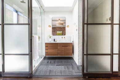 Inspiration for a modern ensuite bathroom in New York with flat-panel cabinets, medium wood cabinets, an alcove shower, white tiles, ceramic tiles, white walls, slate flooring, a submerged sink, marble worktops, grey floors and a hinged door.