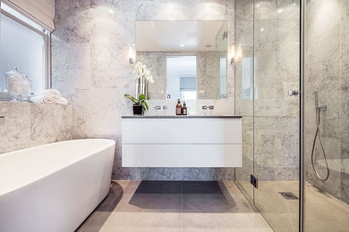Inspiration for a medium sized classic ensuite bathroom in London with freestanding cabinets, white cabinets, a freestanding bath, a walk-in shower, grey tiles, marble tiles, grey walls, porcelain flooring, a built-in sink, grey floors and a hinged door.