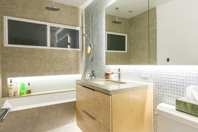 Trendy mosaic tile tub/shower combo photo in Los Angeles with an undermount sink, flat-panel cabinets, light wood cabinets, limestone countertops and an undermount tub