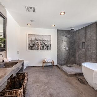 Example of a large trendy master gray tile and cement tile gray floor and concrete floor bathroom design in Los Angeles with white walls, a trough sink, gray countertops, open cabinets, a wall-mount toilet and concrete countertops