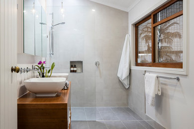 Foto på ett mellanstort funkis en-suite badrum, med öppna hyllor, skåp i mellenmörkt trä, en öppen dusch, grå kakel, porslinskakel, vita väggar, klinkergolv i porslin, träbänkskiva, grått golv och med dusch som är öppen