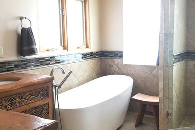 Ejemplo de cuarto de baño de estilo americano de tamaño medio con bañera exenta, sanitario de una pieza, baldosas y/o azulejos beige, baldosas y/o azulejos de vidrio laminado, paredes beige, suelo de baldosas de porcelana y encimera de madera