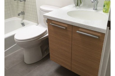 Photo of a medium sized contemporary bathroom in Hawaii with flat-panel cabinets, medium wood cabinets, a one-piece toilet, grey tiles, porcelain tiles, white walls, porcelain flooring, an integrated sink, solid surface worktops and an alcove bath.